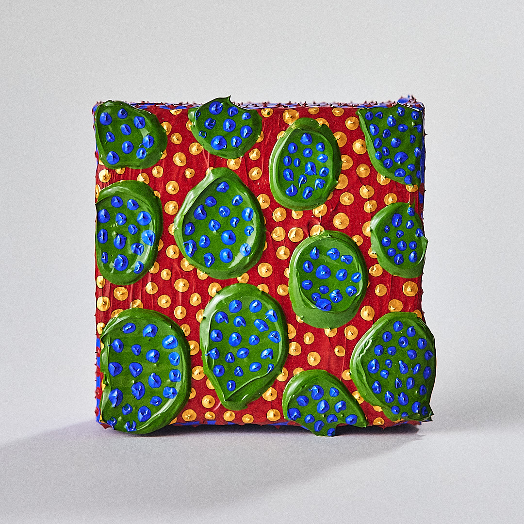 Green rounded shapes with raised blue dots sit against a red and gold painted surface.